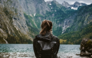 woman in black leather jacket standing on rock near body of water during daytime