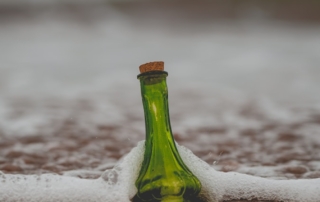 green glass bottle with cork lid on shore